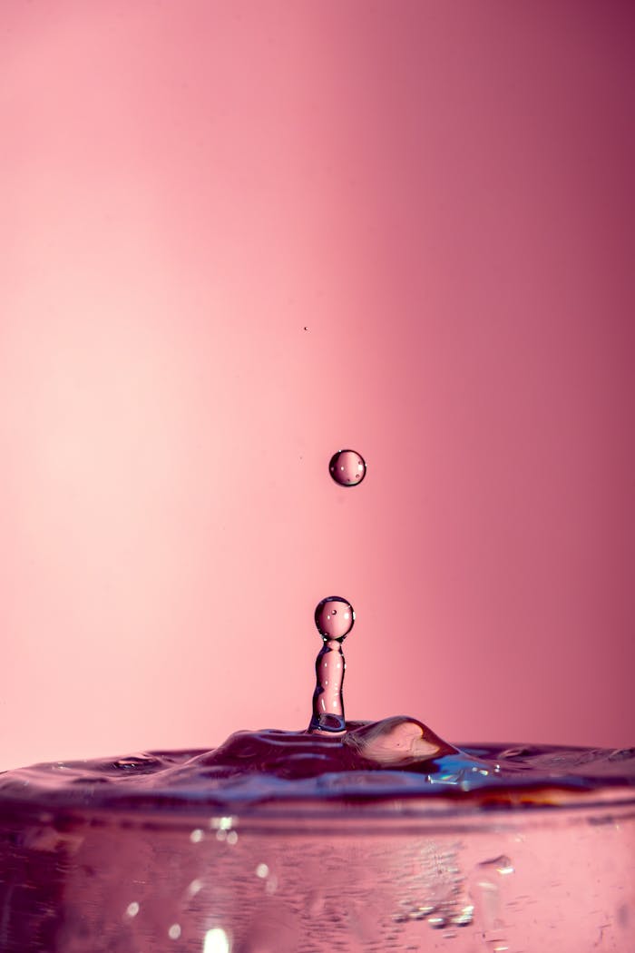A mesmerizing shot of a water droplet captured mid-air against a pink backdrop, showcasing dynamic motion.
